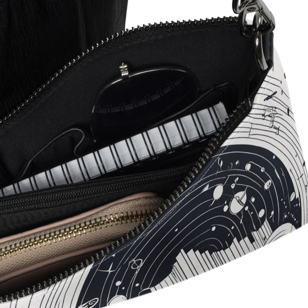 An open black-and-white crossbody bag featuring an abstract geometric design with circular patterns and fine lines. Inside, the bag holds black sunglasses, a striped notebook, and a beige zippered wallet—perfect for stylish everyday use